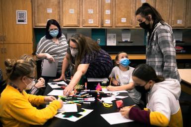 Four middle school girls work on creating paper models of shapes like pyramids, cubes and dodecahedrons with the help of Dr. 玛格丽特·沃茨博士. 芭芭拉·詹宁斯·赫尔佐格, 谁在十大网络娱乐平台注册教数学, 和Bailee back, a junior elementary and special education major. They are in one of the classrooms in Doane's Lied science building. 